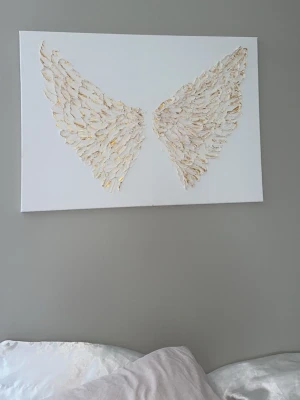 Änglavingar tavla med guld - Unik tavla med 3D-effekt föreställande änglavingar i vitt med inslag av guld på vit canvas. Perfekt som dekoration till sovrum eller vardagsrum. Tavlan har en modern och stilren känsla med struktur i vingarna. (Vid förfrågning kan helvit och silvrig tavla fixas. Även olika färger på bakgrund och övrigt)