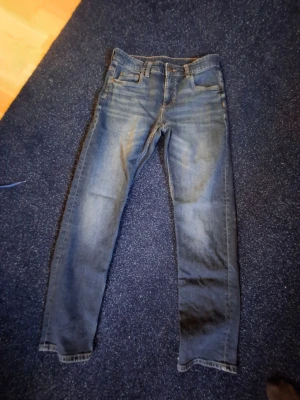 Blå regular jeans med tvättade detaljer - Säljer ett par blå regular jeans med snygga tvättade detaljer och klassisk femficksmodell. Jeansen har normal midja och raka ben. Perfekta till en avslappnad stil och passar till det mesta i garderoben.