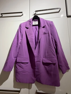 Lila oversized kavaj från ONLY - Snygg lila oversized kavaj från ONLY med klassisk krage, en knapp framtill och två stora fickor. Kavajen har en rak passform . Perfekt för att lyfta vilken outfit som helst.