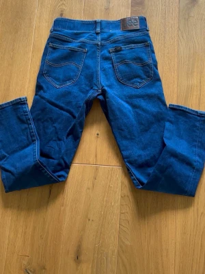 Mörkblå Lee jeans med rak passform - Storlek- w29 L 30.Snygga mörkblå jeans från Lee med klassisk rak passform. Jeansen har Lee-logga på bakfickan och patch i läder. Tillverkade i stretchigt denimtyg för extra komfort. Perfekta för en avslappnad och trendig look.