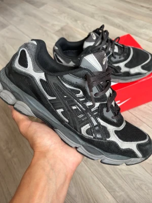  Asics Gel-Nyc - Snygga sneakers från Asics i svart och grå färg med mesh och mockadetaljer. Skorna har en chunky sula och klassisk Asics-logga på sidan. Perfekta för dig som gillar sportig och trendig stil.