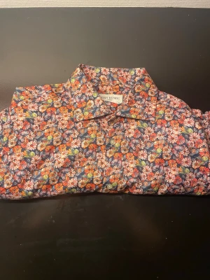 Blommig skjorta från John Henric - Färgstark skjorta från John Henric med blommigt mönster i rött, blått, vitt, grönt och gult. Klassisk krage och knäppning framtill. Perfekt för dig som vill sticka ut med en unik och lekfull stil. Tillverkad i mjuk bomull.