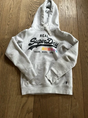Grå superdry hoodie - Jag säljer en riktigt fet Hoodie från superdry, jag säljer den då den är väldigt liten på mig (ca 178). Jag skulle säga att den är i väldigt bra skick utan några defekter. Tröjan satt som bäst på mig när jag var runt 170, men om man gillar att den sitter tight kan man säkert ha den när man är längre. Skriv kring om ni har frågor, jag är villig att diskutera priset.