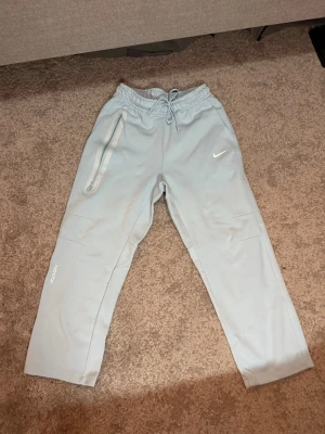 Nocta Byxor Baby Blue - Nocta byxor i baby blue med modern och avslappnad passform. Perfekta för en clean streetwear-look.  Färg: Baby Blue Storlek: S  Fraktar inom 24h vid snabb affär. Byten är inte aktuella.  #Nocta #DrakeNocta #NoctaPants #Streetwear #NikeNoctaNocta byxor i baby blue med modern och avslappnad passform. Perfekta för en clean streetwear-look.  Färg: Baby Blue Storlek: S  Fraktar inom 24h vid snabb affär. Byten är inte aktuella.  #Nocta #DrakeNocta #NoctaPants #Streetwear #NikeNocta