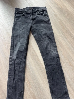 Svarta slim jeans från Nudie Jeans - Säljer ett par svarta slim fit jeans från Nudie Jeans. Jeansen har klassisk femficksmodell, normal midja och raka ben. Materialet är mjukt denim i bomull med snygg tvättad look och subtila slitningar. Perfekta till en avslappnad stil.