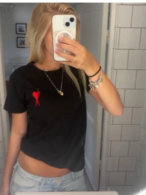 Svart AMI Paris t shirt  - Svart t-shirt med korta ärmar och ett rött hjärta med bokstaven A broderat på bröstet. Enkel och stilren design, perfekt till jeans eller shorts. Tillverkad i mjuk bomull för skön känsla.ej äkta skriv storlek du vill ha så löser jag förmodligen ❤️
