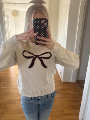 Vit stickad tröja med rosett - Söt vit stickad tröja med en stor mörkröd rosett. Tröjan har rund halsringning, ribbade vid ärmslut och nederkant samt en avslappnad passform. Perfekt till hösten🤍 Aldrig använd, skriv för mer info