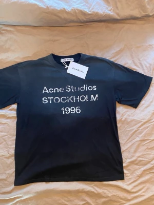Svart Acne Studios t-shirt Stockholm M - Snygg svart t-shirt från Acne Studios med tryck 'Acne Studios STOCKHOLM 1996' på bröstet. Klassisk passform och rund hals. Perfekt till jeans eller shorts för en clean och modern look.