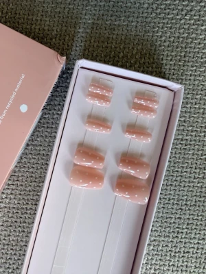 Switch Nails press-on naglar rosa prickiga - Säljer ett set press-on naglar från Switch Nails i en mjuk rosa färg med vita prickar. Naglarna har en oval form och kommer i en snygg förpackning. Tillverkade av återvunnet material och är återanvändbara. Perfekt för dig som vill ha en söt och trendig look.
