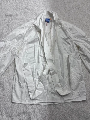 Vit blus med knytband från Crās - Stilren vit blus från Crās med långa ärmar och snyggt knytband vid kragen. Blusen har klassisk skjortkrage och knäppning framtill. Tillverkad i ett lätt och krispigt material som ger en fräsch look.