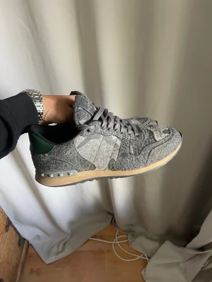 Grå Valentino Rockrunners  - Unika sneakers i grå filtad ull med matchande grå skosnören och beige sula. Skon har en mörkgrön detalj på hälen och coola mönster i materialet. Perfekt för dig som gillar en stilren men ändå annorlunda look.
