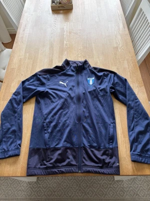 Mörkblå Malmö FF träningströja Puma - Snygg mörkblå träningströja från Puma med Malmö FF-logga på bröstet. Jackan har hel dragkedja, ståkrage och två sidofickor. Tillverkad i ett lätt och funktionellt material som passar perfekt till träning.