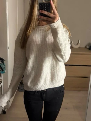 Vit ribbstickad tröja - Klassisk vit ribbstickad tröja med rund hals och långa ärmar. Tröjan har en avslappnad passform och är perfekt för lager på lager. Materialet ser mjukt och bekvämt ut, vilket gör den enkel att styla till olika outfits.