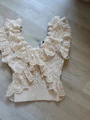 Trendig Zara topp Beige virkad  med volang  - Super trendig topp från Zara .Supersöt beige virkad topp med djup v-ringning och breda volangdetaljer framtill och på axlarna. Toppen är ärmlös och har ett ribbat band nedtill för en snygg passform. Perfekt för dig som gillar romantisk och bohemisk stil,Stockholm stil 