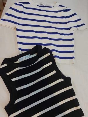 Två randiga toppar i blått och svart - Säljer två snygga toppar: en vit och blå kortärmad topp från Zara och primark med rund hals och ribbad struktur, samt en ärmlös svart och vit randig topp med breda axelband. Perfekta för en trendig och avslappnad look. PRIS KAN DISKUTERAS 