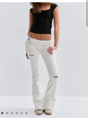 Vita bootcut jeans med slitningar - Snygga vita bootcut jeans med slitningar vid knä och lår. Jeansen har låg midja, fem fickor och broderade detaljer på bakfickorna. Perfekta för dig som gillar en trendig och avslappnad stil.