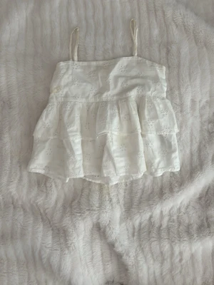 Vit volangtop från Gina Tricot - Söt vit linnetopp från Gina Tricot med tunna axelband och volanger. Toppen har broderade detaljer och är perfekt för sommaren. Lätt och luftig känsla som passar till många olika stilar.❤️💗🫰🏻