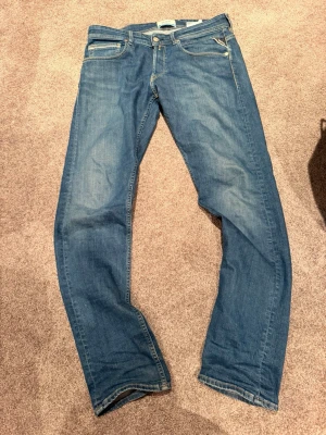 Replay jeans  - Säljer ett par klassiska blå jeans med rak passform och fem fickor. Jeansen har ljusa slitningar framtill och kontrastsömmar. Tillverkade i denim med en snygg tvätt och detaljerade bakfickor med broderi.