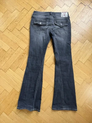 Helt nya tru religon jeans jag har köpt. Jag säljer bara dem för att dem är för små i midjan för mig . Dem är i ett helt nytt skick  - Snygga grå bootcut jeans med lätt slitna detaljer och markerade sömmar. Jeansen har fem fickor, dekorativa bakfickor med lock och knapp samt en klassisk knappgylf. Perfekta för en trendig look.