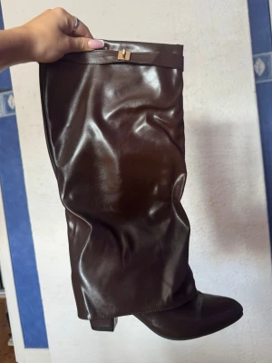 Bruna boots med klack - Snygga bruna boots i glansigt skinnimitation med klack och rundad tå. Stövlarna har en dekorativ rem upptill och en klassisk siluett som passar till många olika outfits. Säljes pga aldrig använt och kommer nog aldrig använda då det var ett impulsköp😅 