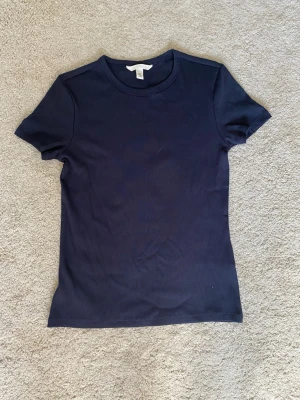 Mörkblå basic t-shirt - En stilren mörkblå t-shirt med rund hals och korta ärmar. Modellen är figurnära och passar perfekt till jeans eller kjol. Tillverkad i mjukt bomullsmaterial för en bekväm känsla hela dagen.