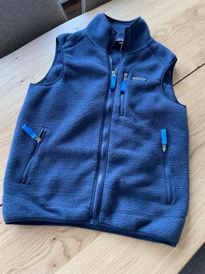 Mörkblå fleeceväst med dragkedjor - Mörkblå fleeceväst från Patagonia med hög krage och tre fickor med dragkedja och blå detaljer. Västen har en mjuk och mysig känsla, perfekt för lager-på-lager och chill dagar. Passar till både jeans och hoodie. Den är i väldigt fint skick. Skriv vid frågor!