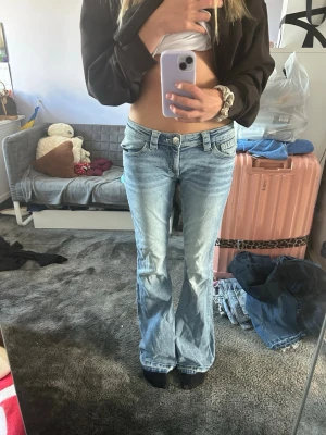  bootcut jeans  - Säljer ett par ljusblå bootcut jeans med låg midja och klassiska fem fickor. Jeansen har slitna detaljer och en avslappnad passform som ger en retro vibe. Perfekta för dig som gillar en casual och trendig stil.