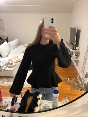 Svart peplum topp med lång ärm - Säljer en svart peplum topp med lång ärm och rund hals. Toppen har en markerad midja och volang nedtill som ger en snygg siluett. Passar perfekt till jeans eller kjol för en trendig look.