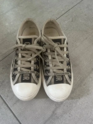Christian Dior sneakers - Snygga sneakers från Christian Dior. Skorna har vita gummisulor, beige snörning och tydlig logga på plösen. Jag köpte dessa på vestiare collective och vet inte riktigt om de är äkta, köpta för 6000☺️ några sömmar har gått upp på sidan men är inget som märks av! Hör av er ifall ni har funderingar💕