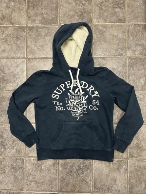 Superdry hoodie med fodrad luva - Riktigt snygg mörkblå dam hoodie från Superdry. Väldigt bra skick. Tröjan är i storlek 36 som motsvarar xs/s. Pris kan diskuteras!
