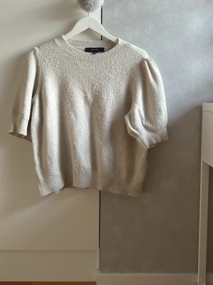 Beige stickad tröja med puffärm - Säljer en beige stickad tröja med korta puffärmar och rund halsringning. Tröjan har ribbade muddar vid ärmslut och nederkant, och är gjord i ett mjukt material som känns skönt mot huden. Perfekt för dig som gillar en enkel men trendig look. Storleken är XL men det är en ganska liten storlek jag har använt den någon gång och är 175 och är perfekt för mig. 