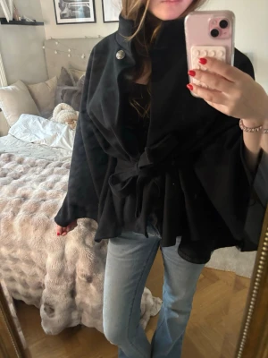 Svart kappa  - Snygg svart kappa med hög krage, vida ärmar och knytband i midjan. Kappan har en guld knapp vid halsen. Skit snyggt till hösten. Köpt för 650kr. Väldigt bra skick. Pris kan diskuteras vid snabbt enkelt köp!🩷