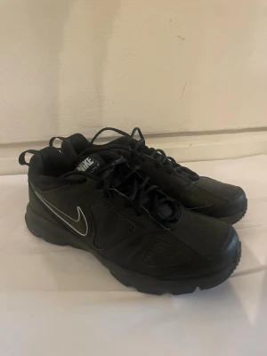 Svarta Nike sneakers med silvrig swoosh - Säljer ett par svarta Nike sneakers med silvrig swoosh på sidan. Skorna har en chunky sula och är gjorda i en mix av läder och syntetmaterial. Klassisk snörning och dragflik bak för enkel påtagning. Perfekta för en sportig och stilren look. Köpte dem för 1200 så tycker 250 är rimligt knappt andvända