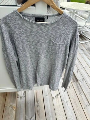 Grå långärmad tröja med ficka - En enkel och stilren grå långärmad tröja från Valient. Tröjan har en liten bröstficka på vänster sida och är tillverkad i ett mjukt material som känns skönt mot huden. Perfekt till jeans eller över en t-shirt för en avslappnad look.