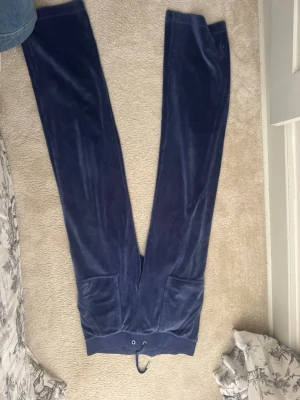 Mörkblå juicy mjukisbyxor - Säljer ett par mörkblå mjukisbyxor i mjuk velour med raka ben och resår i midjan med dragsko. Byxorna har två fickor framtill och en avslappnad passform. Perfekta för chill dagar hemma eller när du vill vara extra bekväm.