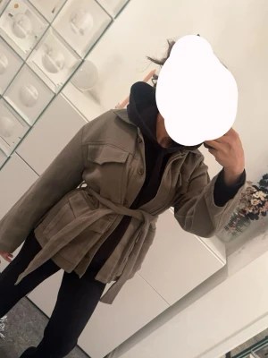 Khaki overshirt med bälte - Stilren khaki overshirt i manchester med knappar framtill och bälte i midjan. Jackan har stora bröstfickor och lång ärm, perfekt för lager på lager under vår och höst.