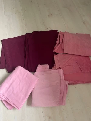 Tygpaket i vinrött och rosa - Säljer ett blandat tygpaket med flera olika tygbitar i vinrött, ljusrosa och gammelrosa. Tygerna är av bomull och manchester, perfekta för sömnadsprojekt, DIY eller lapptäcken. Flera olika storlekar och nyanser ingår.de väger ca 1.300 g