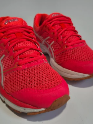 Rosa Asics sneakers - Snygga sneakers från Asics i en stark rosa färg med vita detaljer. Ovandelen är i ventilerande mesh och syntetmaterial, vilket gör dem lätta och bekväma. Klassisk snörning och låg profil. Perfekta för dig som vill sticka ut med färg på fötterna.
