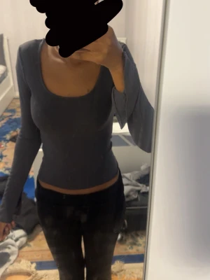 Mörkgrå långärmad croppad topp - Snygg mörkgrå långärmad topp med croppad passform och djup rundad ringning. Ärmarna har en slitsdetalj som ger en cool touch. Perfekt att styla med jeans eller kjol för en trendig look.