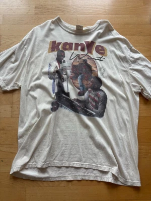 Vit Kanye West t-shirt Comfort Colors - Säljer en vit oversized t-shirt från Comfort Colors med stort Kanye West-tryck på framsidan. T-shirten är i 100% bomull och har korta ärmar samt en klassisk rund hals. Perfekt för dig som gillar streetwear och vill sticka ut med ett snyggt motiv.