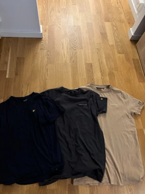 3-pack Lyle & Scott t-shirts - Säljer tre snygga t-shirts från Lyle & Scott i färgerna marinblå, svart och beige. Alla har korta ärmar, rund hals och den klassiska loggan broderad på bröstet. Perfekta för en clean och stilren look.