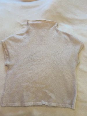 Beige stickad polotröja - Mjuk och enkel beige stickad polotröja med korta ärmar och hög krage. Perfekt för lager på lager och har en avslappnad passform. Materialet ser ut att vara ull eller en ullblandning för extra värme.