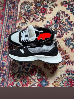 Svarta och vita sneakers med mönster - Snygga sneakers i svart och vitt med grått mönster på sidan. Skorna har vita snören, svart mockadetalj och en tjock vit sula. Ovandelen är i mesh och mocka för en modern look. Perfekta för dig som gillar stilrena men ändå unika sneakers.
