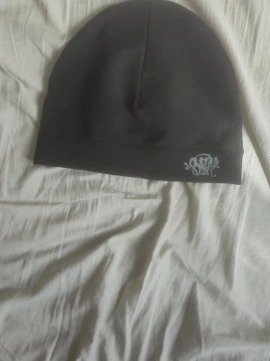 Svart mössa från SYNA - Svart mössa från SYNA med broderad logga framtill. Tillverkad i mjukt och stretchigt material som sitter skönt på huvudet. Enkel och stilren design som passar till det mesta. Perfekt accessoar för kalla dagar.