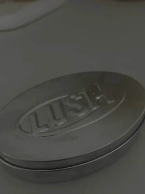 LUSH massagebar i coconut drench - Endast testad en gång. 170 för burken och massage baren. Som igentligen hade kostat 230 Köpt för några dagar sedans  Säljer en oval metallåda från LUSH med en fast kroppsolja inuti. Lådan är silverfärgad och har LUSH-loggan präglad på locket. Kroppsoljan är ljusgul och har ett dekorativt mönster på ytan. Perfekt för dig som gillar fasta produkter och enkel förvaring.