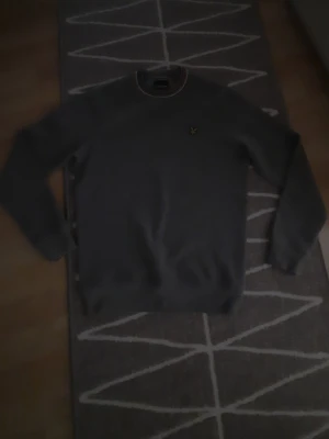 Mörkgrå sweatshirt från Lyle & Scott - Snygg mörkgrå sweatshirt från Lyle & Scott med rund halsringning och klassisk gul logga på bröstet. Tröjan har ribbade muddar vid ärmslut och nederkant samt diskreta ränder i halsen. Perfekt till en avslappnad stil.