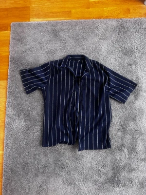 Mörkblå randig kortärmad skjorta - Snygg mörkblå skjorta med vita vertikala ränder och korta ärmar. Skjortan har klassisk krage och knäppning framtill. Perfekt för en avslappnad och trendig stil.
