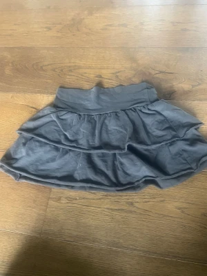 Mörkgrå volangkjol från H&M - Supersöt mörkgrå kjol från H&M med dubbla volanger. Kjolen är kort och gjord i mjuk bomull, perfekt för en avslappnad och trendig look.😍