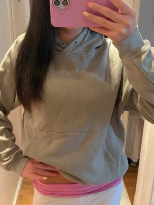 Grå hoodie från Lindex - Säljer en enkel och stilren grå hoodie från Lindex i storlek L. Hoodien har huva med dragsko, magficka och ribbade muddar vid ärmslut och nederkant. Perfekt för en avslappnad look och gjord i mjukt bomullsmaterial.