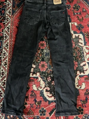 Svarta jeans från Replay - Säljer ett par svarta jeans från Replay med raka ben och klassiska bakfickor. Jeansen har en snygg tvättad look och är tillverkade i bomullsmix. Perfekta för dig som gillar en avslappnad men stilren vibe.